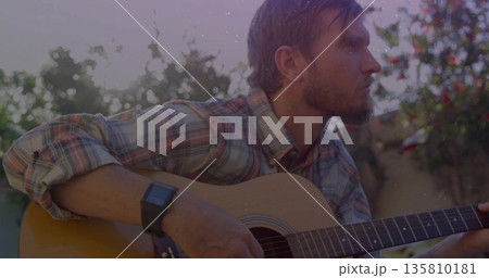 Playing musician wearing plaid shirt strumming acoustic guitar in garden at sunset, with smartwatch Playing musician wearing plaid shirt strumming acoustic guitar in garden at sunset, with smartwatch 135810181