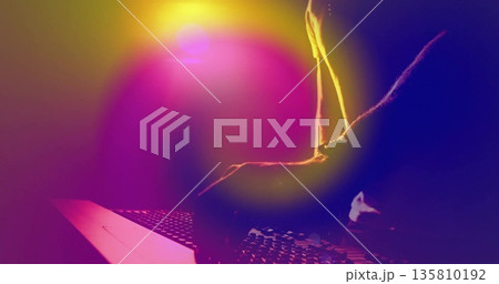 Leaning adult male typing on laptop keyboard at studio desk, with neon light glow, copy space 135810192