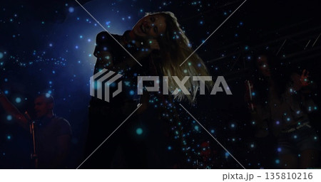 Swaying singer wearing black top holding microphone on stage under blue confetti and stage lighting Swaying singer wearing black top holding microphone on stage under blue confetti and stage lighting 135810216