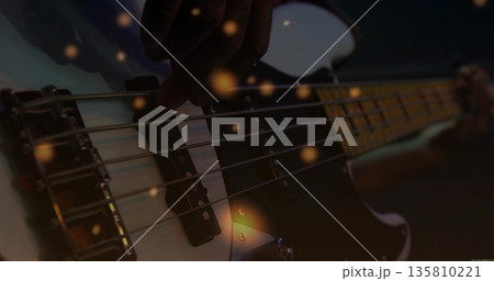 Plucking adult musician's fingers gliding over bass guitar strings on stage, with bokeh and pickups 135810221