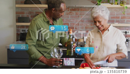 Senior couple cooking together in modern home kitchen, with wine bottle and red peppers 135810739