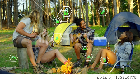 Friends playing guitar, holding beer bottles at campfire in forest clearing, with yellow or blue ten 135810779