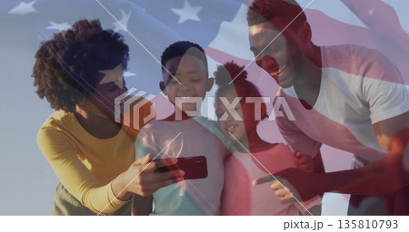 Standing family of four wearing T-shirts sharing smartphone outdoors, with American flag overlay Standing family of four wearing T-shirts sharing smartphone outdoors, with American flag overlay 135810793