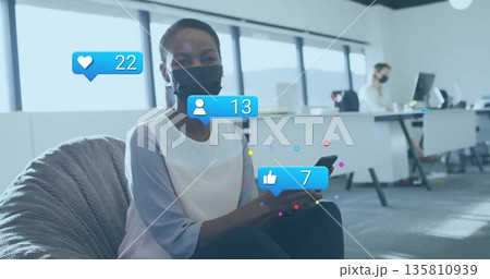 Holding smartphone masked office worker scrolling feed in lounge area with overlay icons Holding smartphone masked office worker scrolling feed in lounge area with overlay icons 135810939