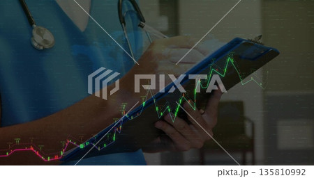 Writing on clipboard clinician wearing scrubs and stethoscope in clinic with digital graph overlay 135810992