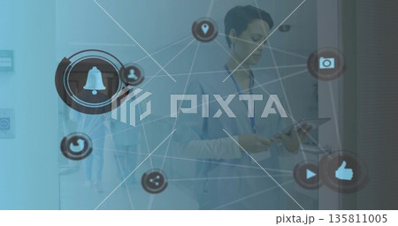 Consulting nurse wearing blue scrubs holding tablet in hospital corridor, using connectivity icons 135811005