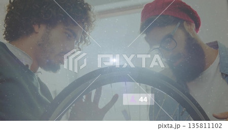 Two men examining spokes on bicycle wheel in repair workshop, with digital overlay showing 44 Two men examining spokes on bicycle wheel in repair workshop, with digital overlay showing 44 135811102