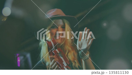 Musician shaking red tambourine and waving under stage lights, with wide-brimmed hat and bracelets 135811130