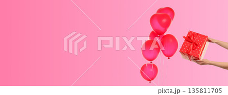 Red balloons float upward while a gift box with a red bow is held 135811705
