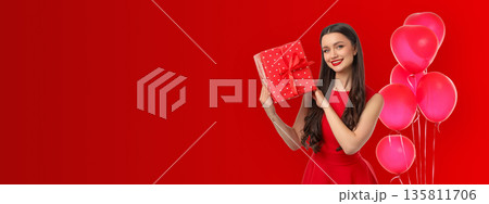 Young woman in a red dress smiles while holding a gift box 135811706