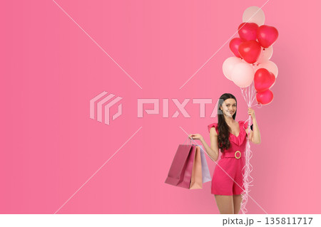 Woman in pink holds heart balloons and bags 135811717