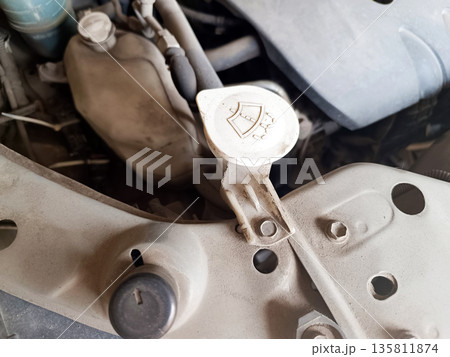 Close-up of a very dusty car engine bay, highlighting the windshield washer fluid reservoir cap with its distinct shield and spray icon. Maintenance needed Close-up of a very dusty car engine bay, highlighting the windshield washer fluid reservoir cap with its distinct shield and spray icon. Maintenance needed 135811874