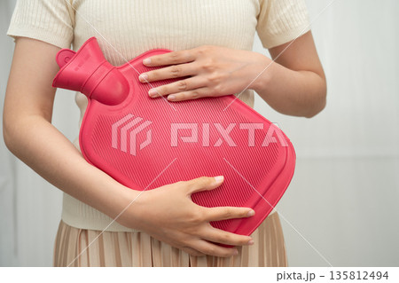 Woman using hot water bottle to relieve menstrual abdominal pain. Woman using hot water bottle to relieve menstrual abdominal pain. 135812494
