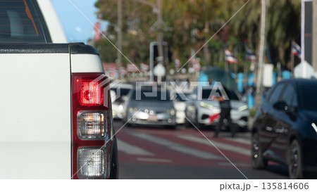 Rear side of pickup car with turn on brake light. Stop to let pedestrians cross at the red and white crosswalk. Were many cars parked in a row on the opposite road. Traffic in Thailand is like that. 135814606