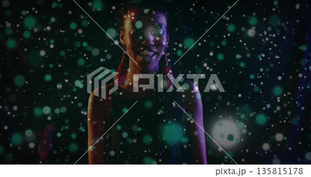 Performing artist wearing red tassel earrings standing on stage, under green and white light spots Performing artist wearing red tassel earrings standing on stage, under green and white light spots 135815178