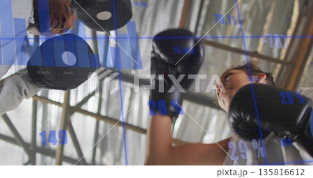 Practicing boxer wearing boxing gloves and white top punching focus mitts in gym, with data overlay 135816612