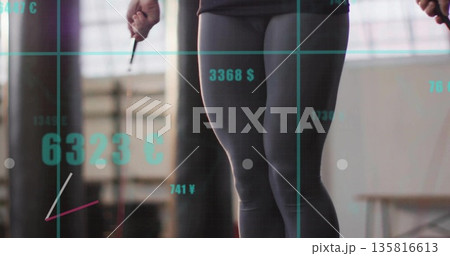 Jumping woman in athletic wear at gym studio, with punching bag, jump rope, teal currency grid 135816613