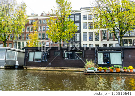 A floating house in Amsterdam canal. Boat home on water. Houseboat in Netherlands 135816641