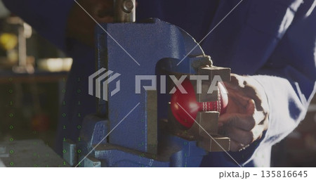 Coverall-clad technician clamping baseball in blue metal vise at shop workbench, with blurred tools 135816645
