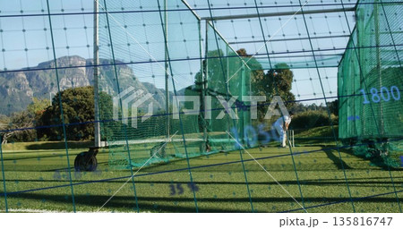 Swinging male golfer wearing polo, hitting golf ball inside calibrated net cage on turf, copy space Swinging male golfer wearing polo, hitting golf ball inside calibrated net cage on turf, copy space 135816747