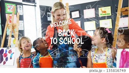 Guiding female art teacher directing children painting on easels in art room, with colorful aprons Guiding female art teacher directing children painting on easels in art room, with colorful aprons 135816749