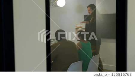 Holding open magazine, presenter briefing coworkers at meeting table by flat-screen, copy space Holding open magazine, presenter briefing coworkers at meeting table by flat-screen, copy space 135816768