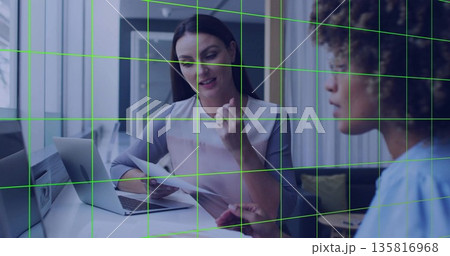 Discussing printed documents, two colleagues gesturing and listening in meeting room with laptop Discussing printed documents, two colleagues gesturing and listening in meeting room with laptop 135816968