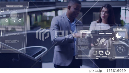 Pointing toward digital dashboards in office atrium, two colleagues in suits analyzing data charts Pointing toward digital dashboards in office atrium, two colleagues in suits analyzing data charts 135816969