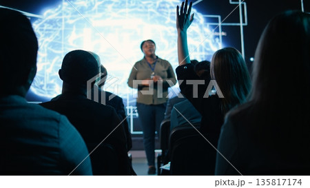Girl in audience interacting with black female speaker presenting AI systems at business convention, showing automation and AI brain visuals for software development. Active participants. 135817174