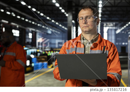 Warehouse employee checks construction tools near heavy metal equipment, managing industrial operation and production workflow with machinery. Workforce maintaining manufacturing process. Warehouse employee checks construction tools near heavy metal equipment, managing industrial operation and production workflow with machinery. Workforce maintaining manufacturing process. 135817216