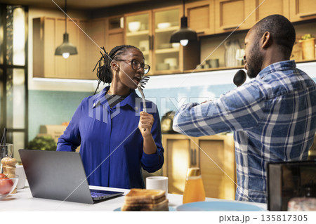 Smiling girlfriend and boyfriend enjoying karaoke in the kitchen. African American partners sing and dance with goofy enthusiasm, creating a romantic funky morning filled with laughter. 135817305