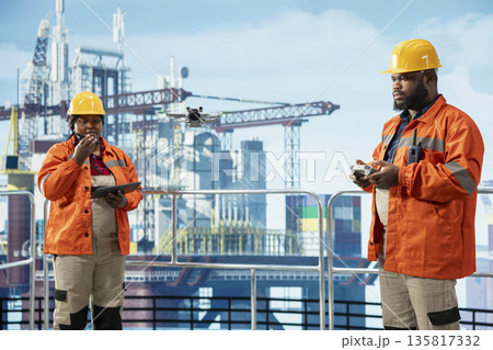 Technicians working together on offshore platform, doing site inspection using drone. Coworkers use aerial photography tech to determine optimal locations for drilling pipelines Technicians working together on offshore platform, doing site inspection using drone. Coworkers use aerial photography tech to determine optimal locations for drilling pipelines 135817332