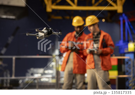 Selective focus of colleagues using a drone for surveillance from offshore oil rig platform, mapping fuel extraction perimeter and ensuring efficient oil industry inspection. Remote control. Selective focus of colleagues using a drone for surveillance from offshore oil rig platform, mapping fuel extraction perimeter and ensuring efficient oil industry inspection. Remote control. 135817335
