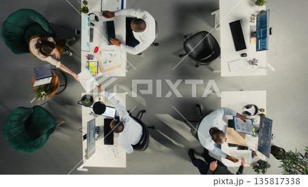 Top down view of business staff in modern office sharing insights and reports, team focuses on data visualization for efficient resource allocation. Company administration. Top down view of business staff in modern office sharing insights and reports, team focuses on data visualization for efficient resource allocation. Company administration. 135817338