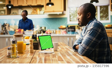 Chroma key display on tablet with African American man at the table, enjoying a casual breakfast at home in the kitchen. Serving healthy food and coffee, illustrating cozy morning. Chroma key display on tablet with African American man at the table, enjoying a casual breakfast at home in the kitchen. Serving healthy food and coffee, illustrating cozy morning. 135817396
