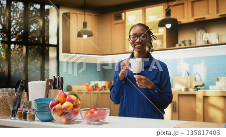 Happy adult in the kitchen smelling the fresh aroma of roasted coffee, serving delicious homemade breakfast. Woman uses prepare slices of toast with croissants and enjoys warm coffee cup. Happy adult in the kitchen smelling the fresh aroma of roasted coffee, serving delicious homemade breakfast. Woman uses prepare slices of toast with croissants and enjoys warm coffee cup. 135817403
