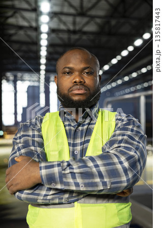 African american plant engineer standing near steel machinery during construction tasks, showcasing production responsibility and the power of fabrication. Hi vis vest for safety at work. African american plant engineer standing near steel machinery during construction tasks, showcasing production responsibility and the power of fabrication. Hi vis vest for safety at work. 135817443