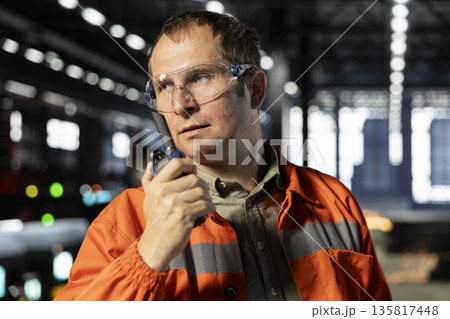 Employee speaking through walkie talkie radio to oversee machinery operation, demonstrating manpower and the professional responsibility in manufacturing process for production. 135817448