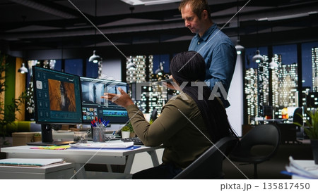 Diverse colleagues working together on video editing for a montage on software, digital media creation. Filmmaker and assistant using dual monitors to edit footage for web content. Camera A. Diverse colleagues working together on video editing for a montage on software, digital media creation. Filmmaker and assistant using dual monitors to edit footage for web content. Camera A. 135817450