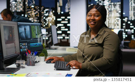 Female expert editor working in video production industry at agency office, doing color grading and creating a montage on dual monitors. Creative process with multimedia tech tools. Camera B. 135817451