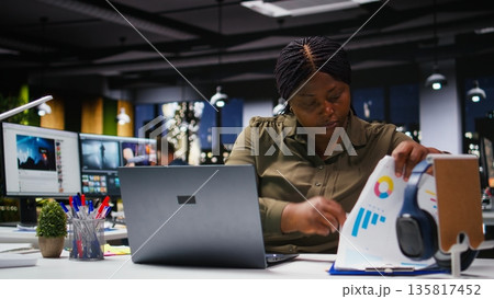 Black company worker checking market research and graphs on a laptop, examining insights and reports for data visualization in the workspace. Resource allocation strategy for goals. Camera A. Black company worker checking market research and graphs on a laptop, examining insights and reports for data visualization in the workspace. Resource allocation strategy for goals. Camera A. 135817452