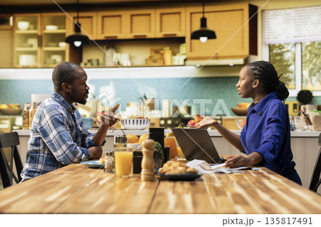 African American couple arguing over bills and debt sitting at the table, frustrated people with receipts and calculator. Financial conflict shows stress, money problems and household tension. African American couple arguing over bills and debt sitting at the table, frustrated people with receipts and calculator. Financial conflict shows stress, money problems and household tension. 135817491