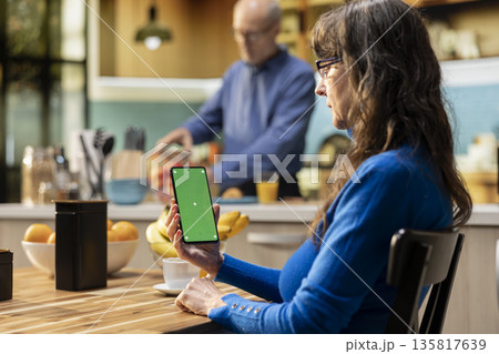 Green screen on mobile phone with pensioner at the breakfast table, retirement lifestyle with healthy food and coffee for cozy atmosphere at home. Senior man checking display. Green screen on mobile phone with pensioner at the breakfast table, retirement lifestyle with healthy food and coffee for cozy atmosphere at home. Senior man checking display. 135817639