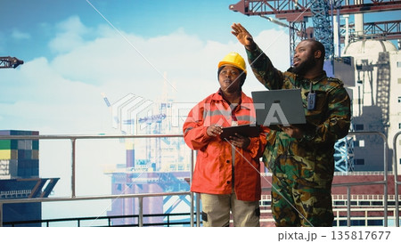 Military personnel stationed on offshore rig analyzing tactical data on laptop. Soldier provides protection to drilling barge, reviewing mission dashboard on notebook, Military personnel stationed on offshore rig analyzing tactical data on laptop. Soldier provides protection to drilling barge, reviewing mission dashboard on notebook, 135817677
