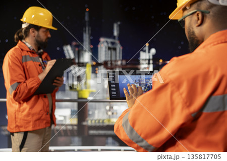 Drilling rig expert analyzing derrick performance on tablet dashboard screen. Offshore platform worker monitoring oil extraction rates and system pressure using device app Drilling rig expert analyzing derrick performance on tablet dashboard screen. Offshore platform worker monitoring oil extraction rates and system pressure using device app 135817705