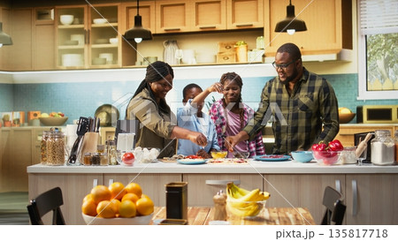 Family fun in the kitchen as everyone is layering cheese and mozzarella on the dough, preparing homemade pizza together. Warm domestic scene captures joy and delicious homemade food. Camera A. Family fun in the kitchen as everyone is layering cheese and mozzarella on the dough, preparing homemade pizza together. Warm domestic scene captures joy and delicious homemade food. Camera A. 135817718