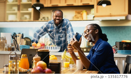 Black girlfriend taking photos of her and boyfriend on the smartphone, laughing and enjoying time together. Happy couple feeling happy in their relationship, joyous woman at home. Black girlfriend taking photos of her and boyfriend on the smartphone, laughing and enjoying time together. Happy couple feeling happy in their relationship, joyous woman at home. 135817776