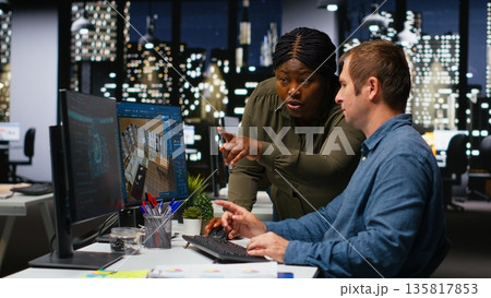 Diverse designers engineers using AI neural networks to create interior design of a new apartment building, architectural software for a floor plan at workstation. Dual monitors. Camera B. 135817853