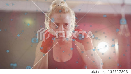 Standing boxer holding fists in boxing gym, with dark tank top, red wraps, network icons Standing boxer holding fists in boxing gym, with dark tank top, red wraps, network icons 135817868