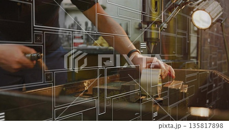 Operating machinist gripping workpiece under drill press in metal shop, digital overlays 135817898